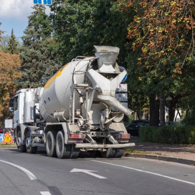 Concrete mixer truck on the road with trees in autumn colors and a clear sky in the background.